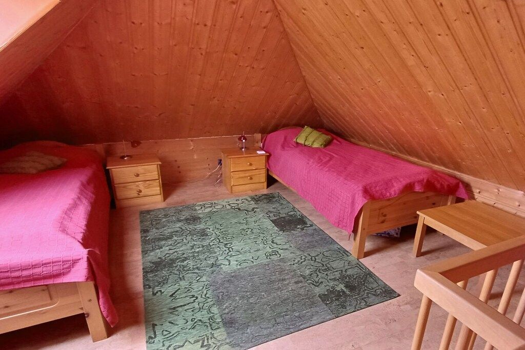 Une petite chambre mansardée, chaleureuse et accueillante, avec deux lits, une commode en bois, une petite table et un tapis à motifs.