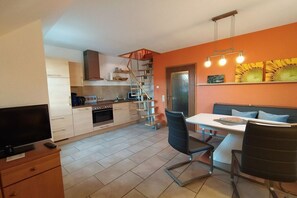 A compact kitchen with a dining area, a TV, and a staircase leading to a loft. - House on Häfchenweg Apartment 6 (Cuxhaven)