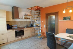 Eine kleine Küche mit Backofen, Mikrowelle und Gaskochfeld. Eine Holztreppe führt zu einer Schlafgalerie.