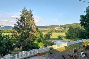 Vistes d'un paisatge rural amb una valla blanca de palets, un arbre gran i un cel serè.
