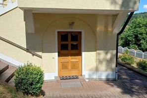 Entrada d'un edifici amb una porta de fusta, un petit porxo i un camí de maó que condueix a l'entrada.