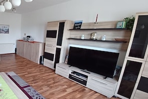 A modern living room with a large flat-screen TV, built-in shelving, and a wooden cabinet. - Jendrusiak holiday apartment (Krayenberggemeinde)