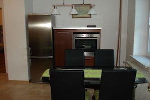 A compact kitchen with a refrigerator, oven, and dining table with chairs. - Jendrusiak holiday apartment (Krayenberggemeinde)