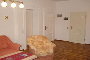 A room with a wooden floor, a sofa, a patterned armchair, and a door with a small picture on the wall. - Jendrusiak holiday apartment (Krayenberggemeinde)
