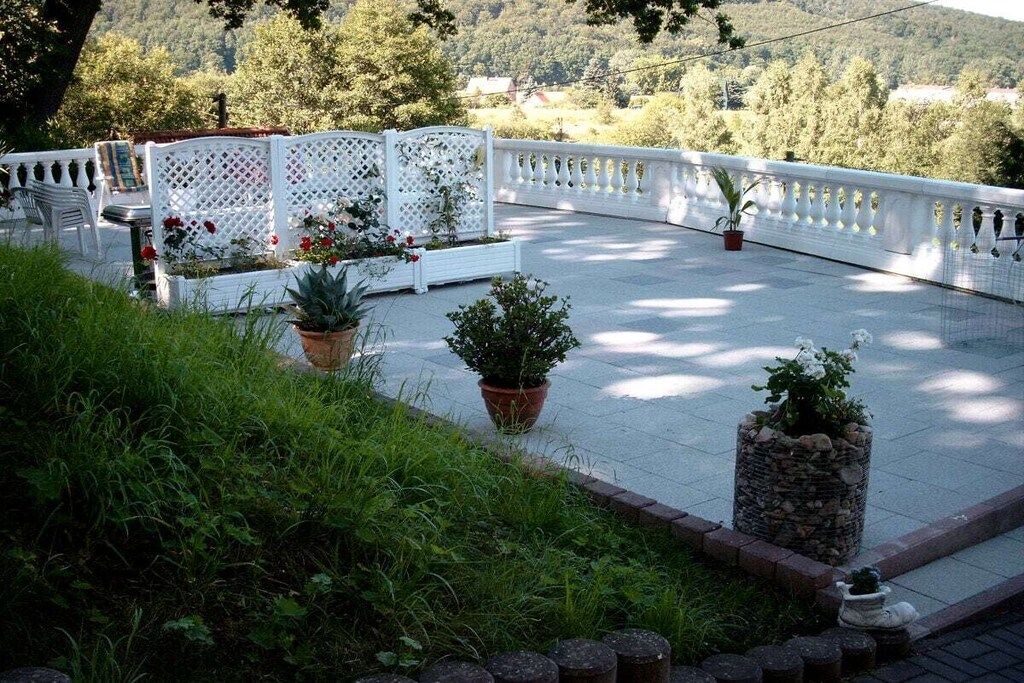 A rooftop terrace with a white lattice fence, potted plants, and a view of the surrounding landscape.