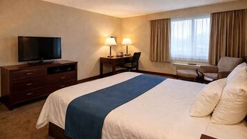 Una habitación de hotel con cama, escritorio con silla, televisor y ventana con cortinas.