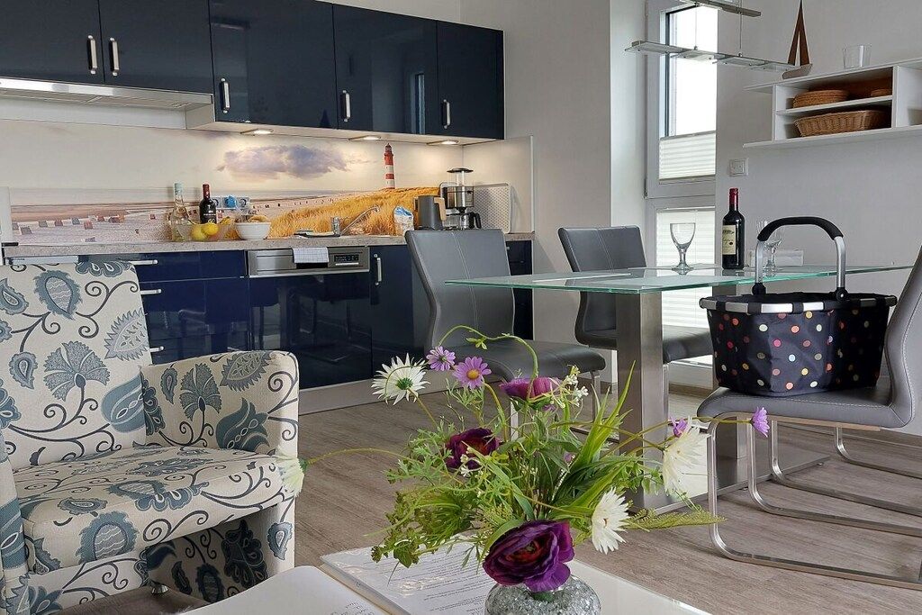 Een moderne keuken met donkere kastjes, een glazen eettafel en een bloemstuk.
