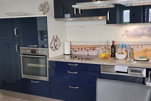 A modern kitchen with a built-in oven, a coffee machine, and a wine bottle on the counter. - Holiday apartment with 2 bedrooms (Dorum-Neufeld)