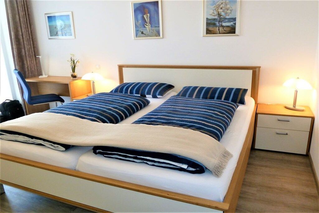 Una habitación de hotel con cama, mesitas de noche, un escritorio y cuadros en la pared.