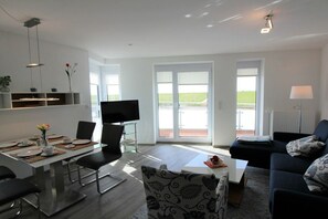 A modern living room with a dining area, a flat-screen TV, and a sofa. - Holiday apartment with 2 bedrooms (Dorum-Neufeld)