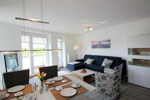 A modern living room with a sofa, coffee table, and dining area set up for a meal. - Holiday apartment with 2 bedrooms (Dorum-Neufeld)