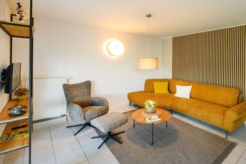 A modern living room with a sofa, armchair, coffee table, and a television on a shelf.