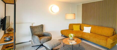 A modern living room with a sofa, armchair, coffee table, and a television on a shelf.