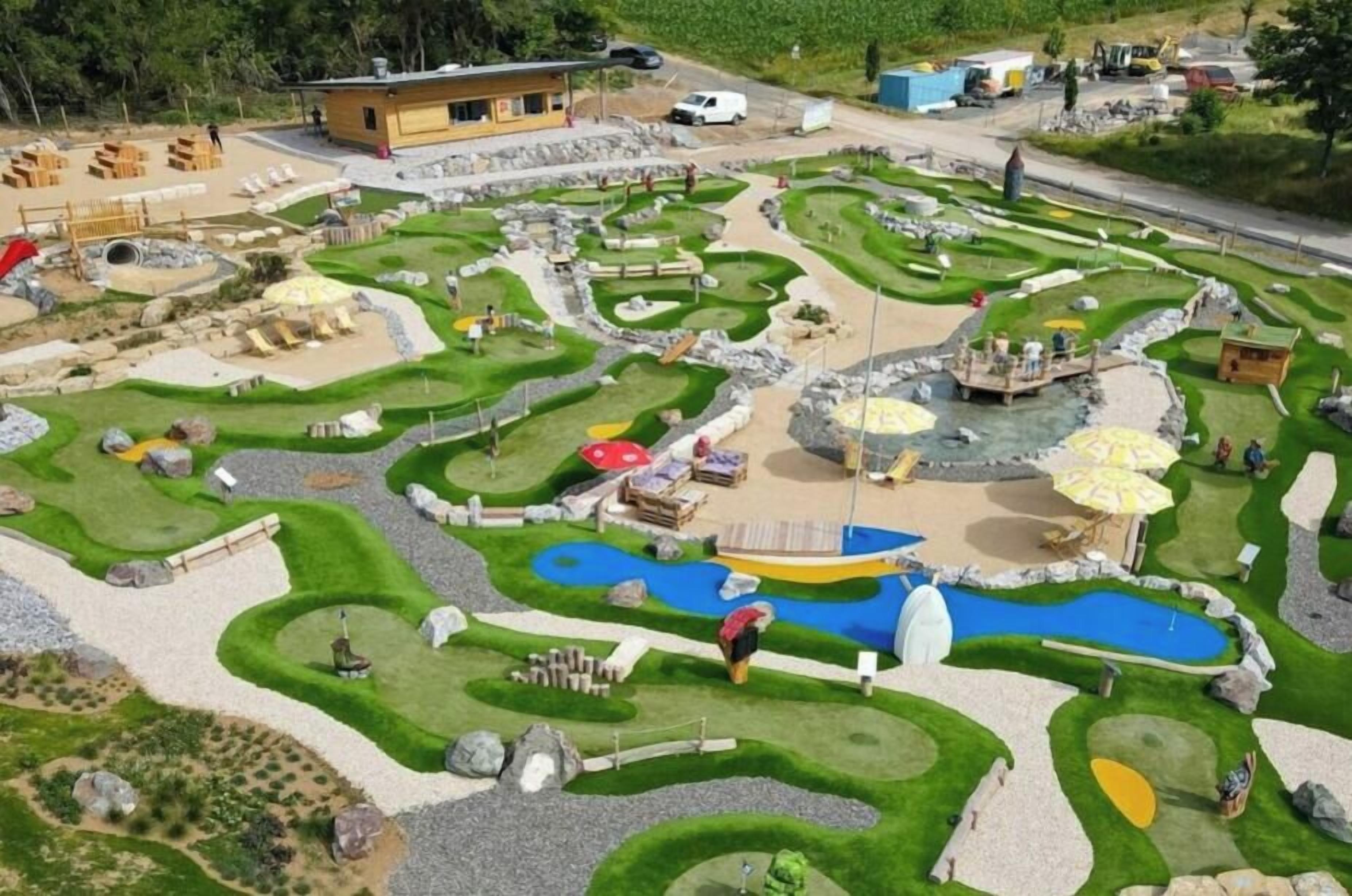 Ein Minigolfplatz mit verschiedenen Bahnen, einem kleinen Pool und Sitzbereichen.