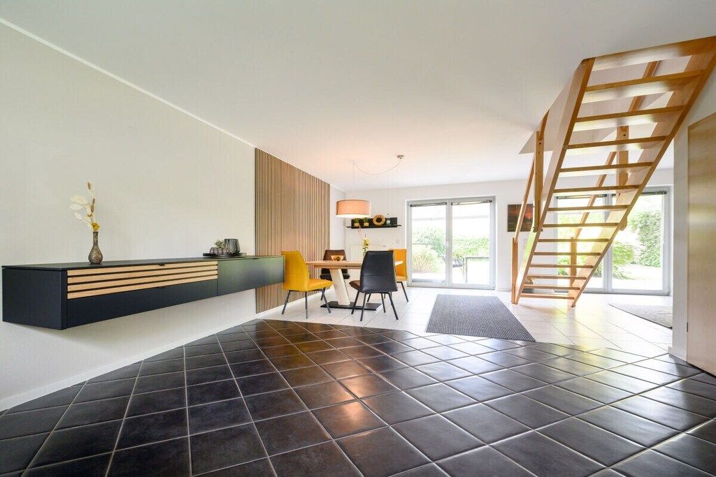A modern interior with a black-tiled floor, a wooden staircase, a dining area with yellow chairs, and a black console table.
