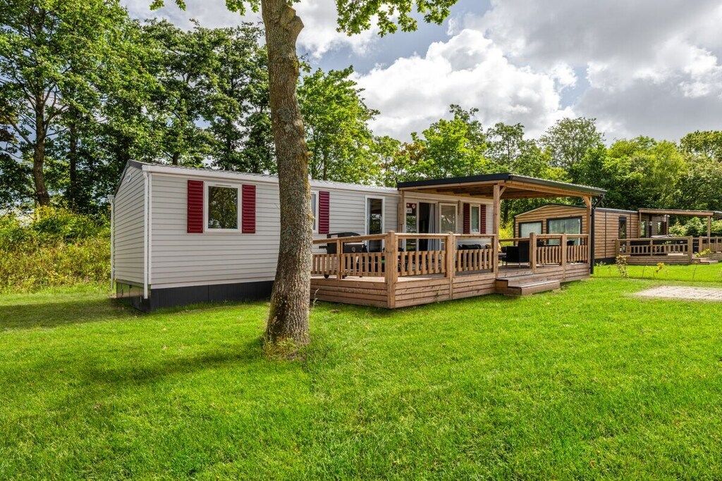 A mobile home with a deck and a covered porch, surrounded by greenery.