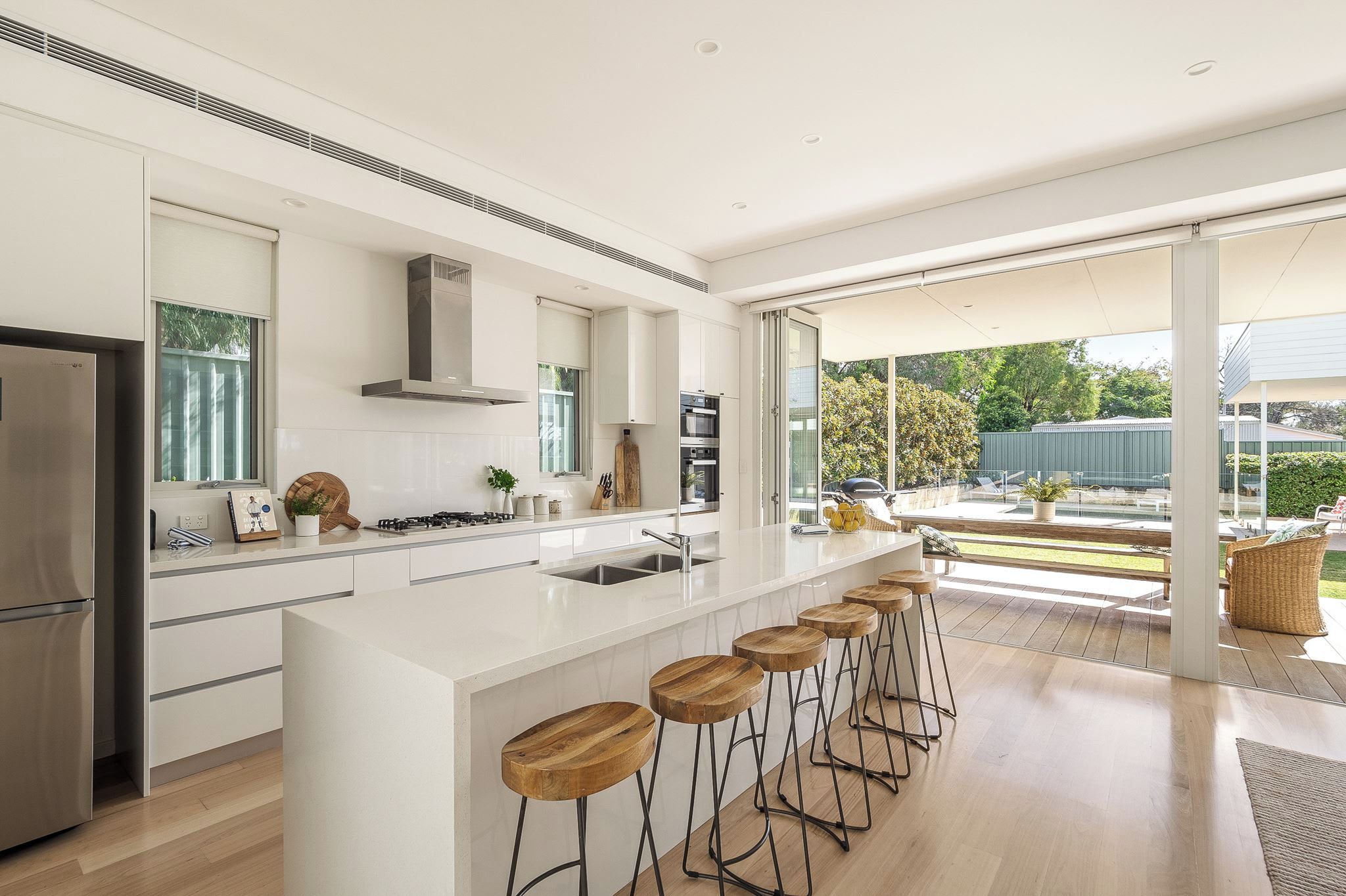 Een moderne keuken met een groot eiland, barstoelen en uitzicht op het buitenterras.