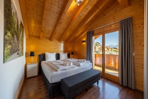 Ein Schlafzimmer einer Holzhütte mit einem Bett, einer Bank, Nachttischen und einem großen Fenster mit Vorhängen.