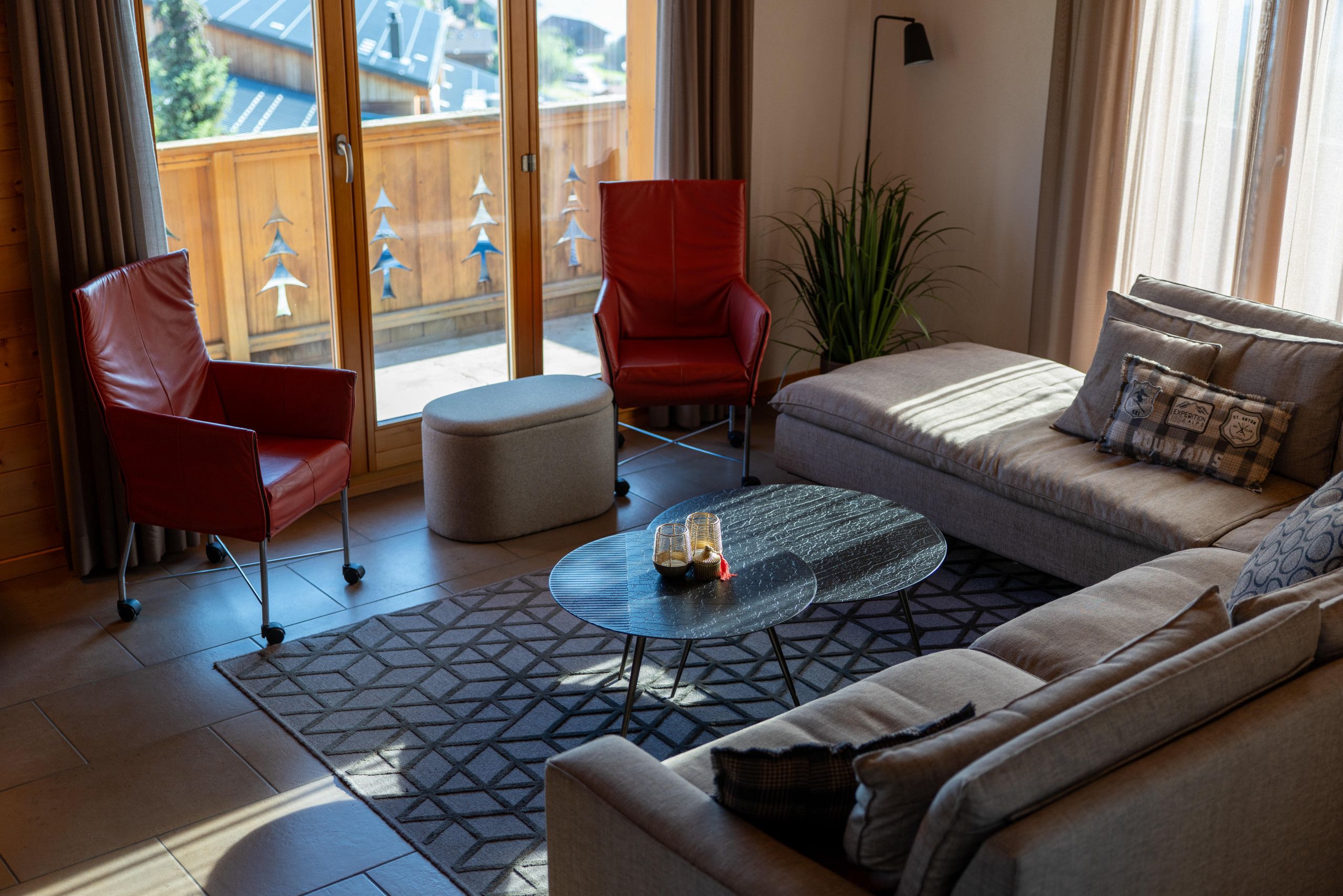Una sala de estar moderna con un sofá, dos sillones rojos, una mesa de centro de vidrio y una alfombra estampada.