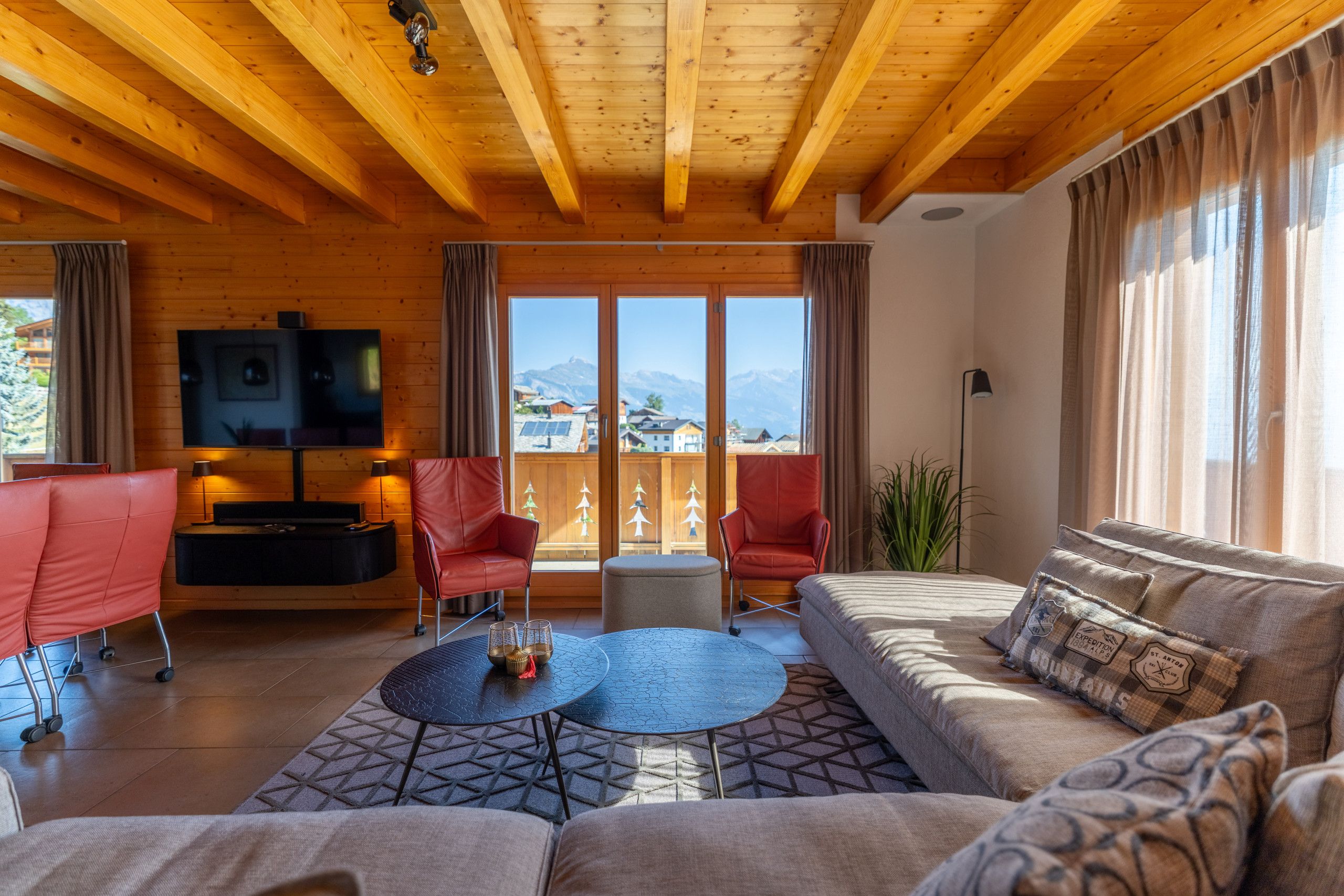 Ein geräumiges Wohnzimmer mit Holzboden, einem großen Fernseher und einem Sofa mit gemusterten Kissen.