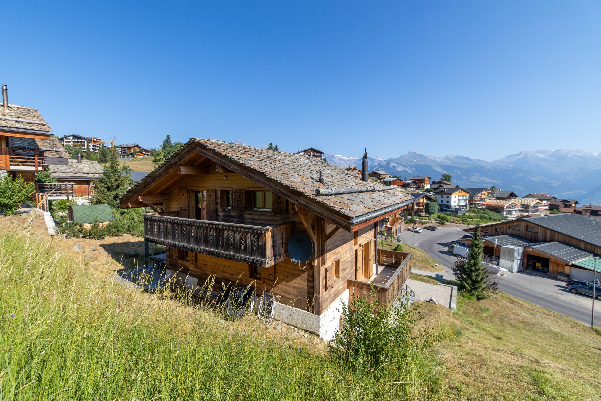 Un chalet en bois doté d’un balcon, entouré d’un paysage vallonné et offrant une vue dégagée sur les montagnes lointaines.
