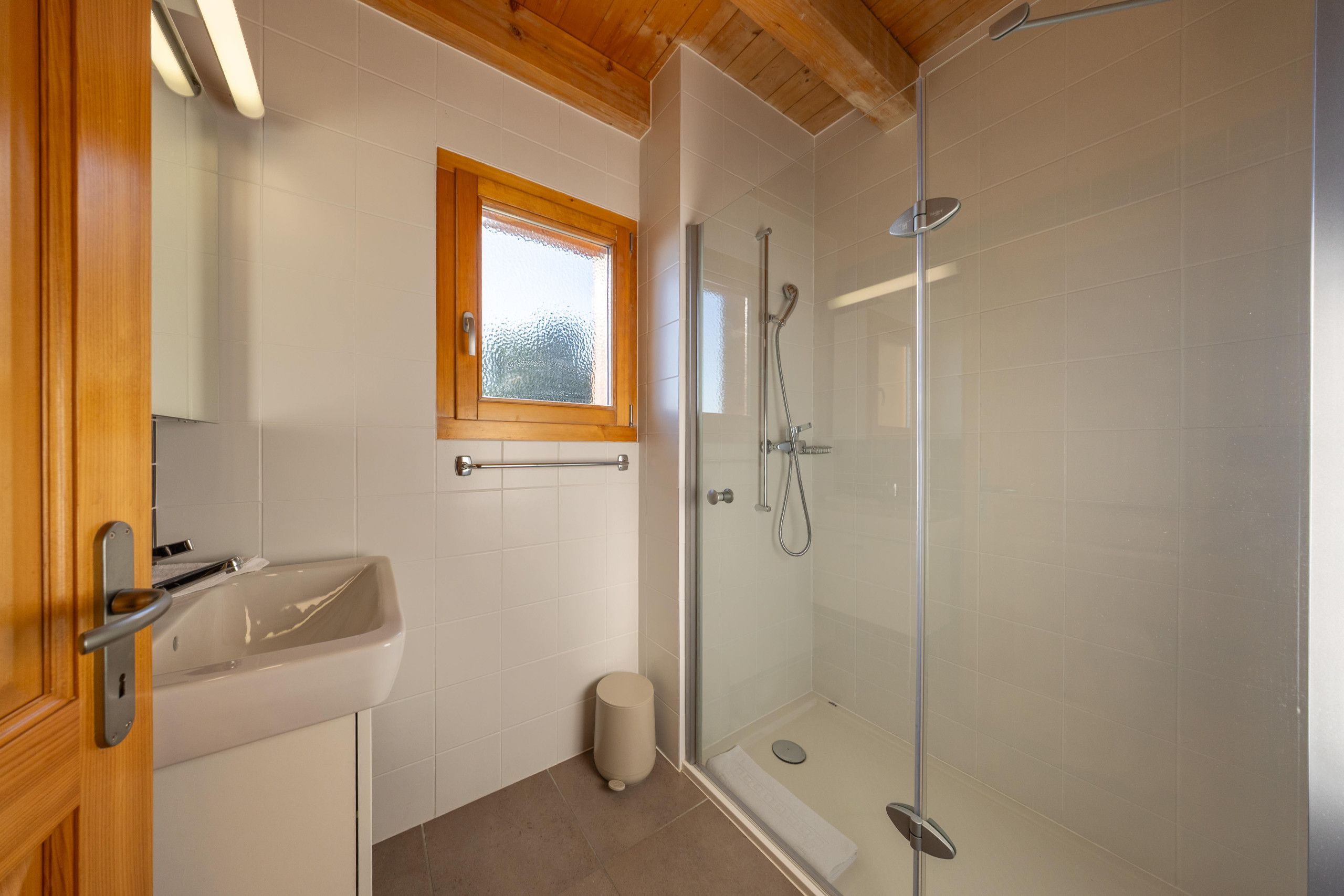 Une salle de bain avec une douche à parois de verre, un lavabo et une fenêtre.