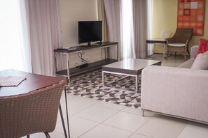 A modern living room with a sofa, a dining table, a TV on a stand, and a patterned rug.