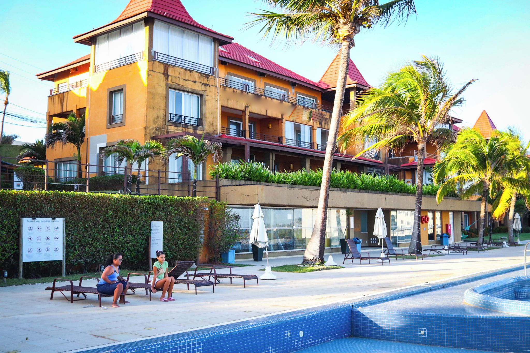 Un hôtel doté d’une piscine, d’un espace extérieur aménagé et de palmiers.