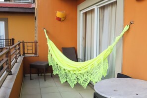Un balcón con una hamaca, una silla, una mesa y un ventanal corredero.