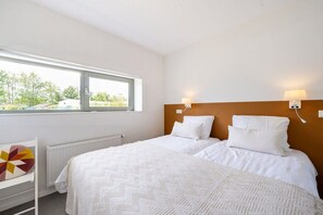 A hotel room with a large window, two beds, a radiator, and a wall-mounted lamp. - Veranda Aan Noordzee (Sint Maartenszee)