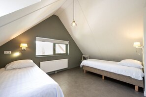 A room with two beds, a window, a radiator, and a hanging light fixture.