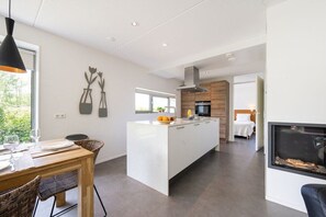 A modern kitchen with a central island, a dining area with a table and chairs, and a living space with a fireplace.