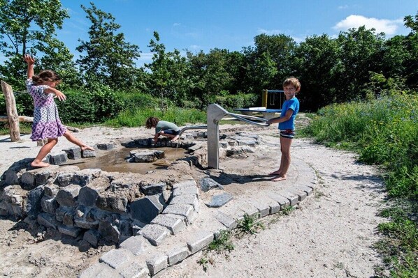 Children playing on a sandy play area with a water feature and a slide.