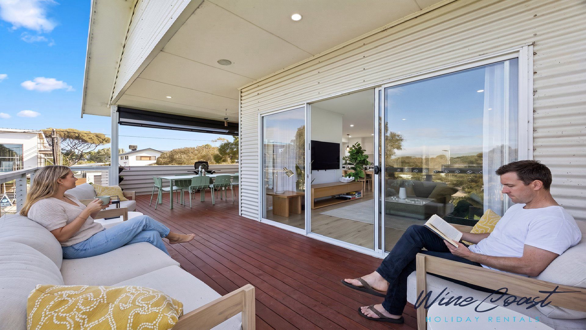 Un área de estar exterior moderna con una terraza de madera, un portón corredizo de vidrio que da a un balcón y un televisor de pantalla plana montado en la pared.