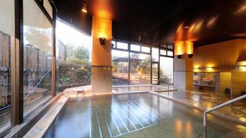 Una piscina interior con paredes de vidrio transparente, suelo de baldosas e iluminación cálida.