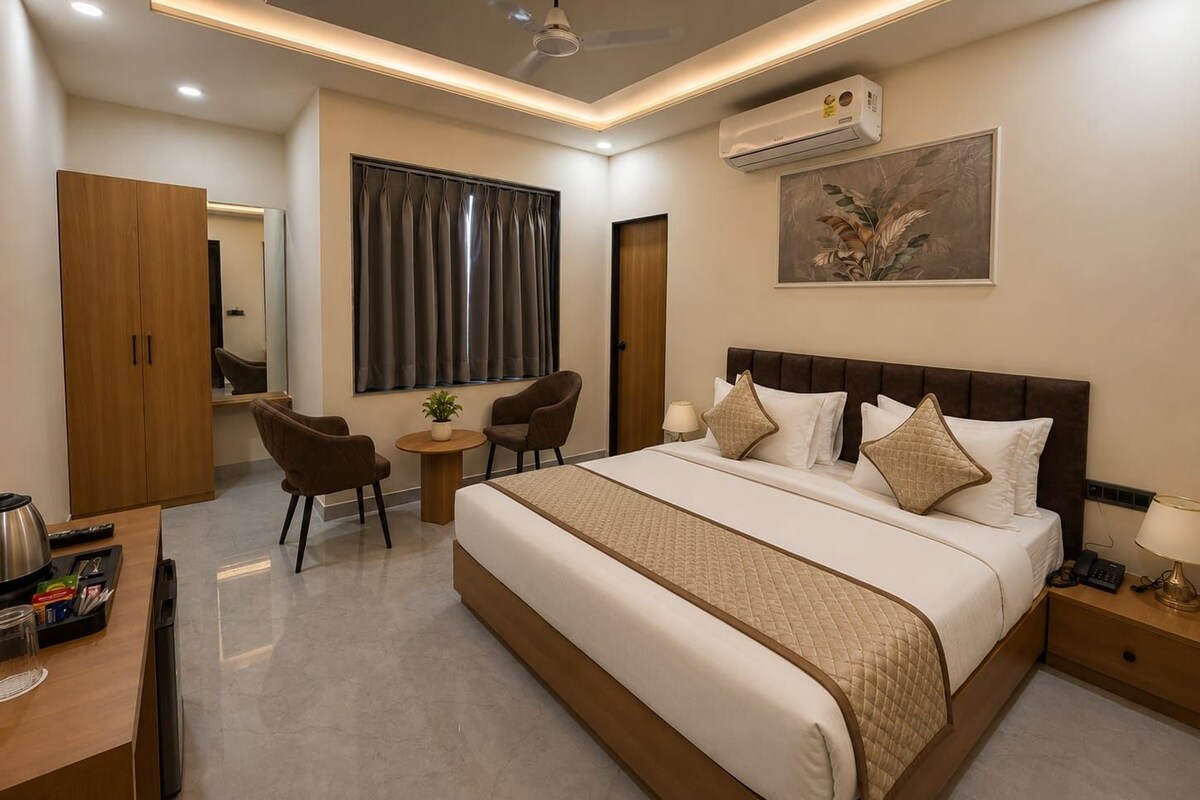 Habitación de hotel con cama, mesita de noche, lámpara, aire acondicionado, ventilador de techo y vistas al exterior a través de una ventana.