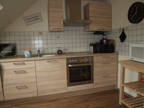 Eine Küche mit Holzausstattung, einem Edelstahlbackofen, einer Mikrowelle und einer Uhr an der Wand.