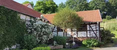 A traditional half-timbered house with a red-tiled roof, surrounded by lush greenery and a well-maintained garden.