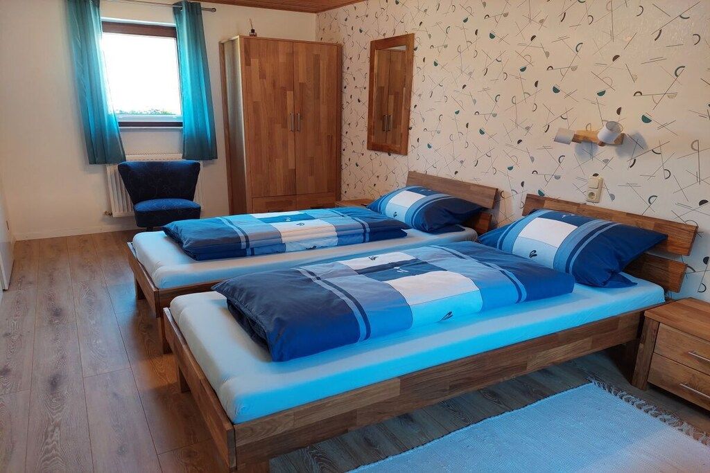 A bedroom with two beds, a wardrobe, a chair, and a window with curtains.