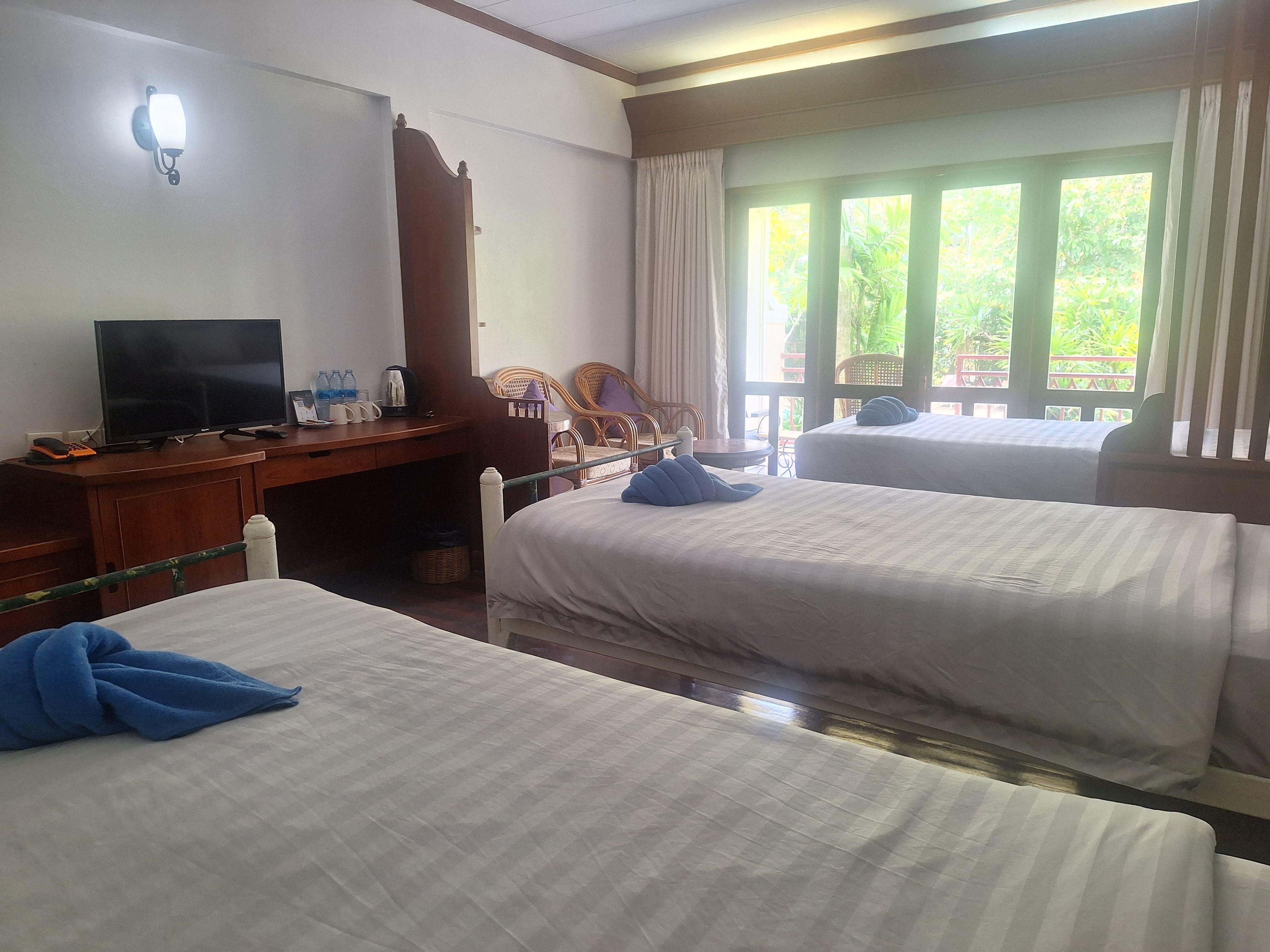 A hotel room with two beds, a desk with a television, and a window with curtains.