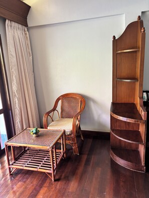 A room with a wooden chair, a small table with a basket, a wooden shelf unit, and a window with curtains.