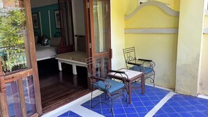 Una habitación con cama, una mesita y sillas, un balcón con azulejos azules, y vista a zonas verdes.