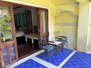 Una habitación con cama, una mesita y sillas, un balcón con azulejos azules, y vista a zonas verdes.