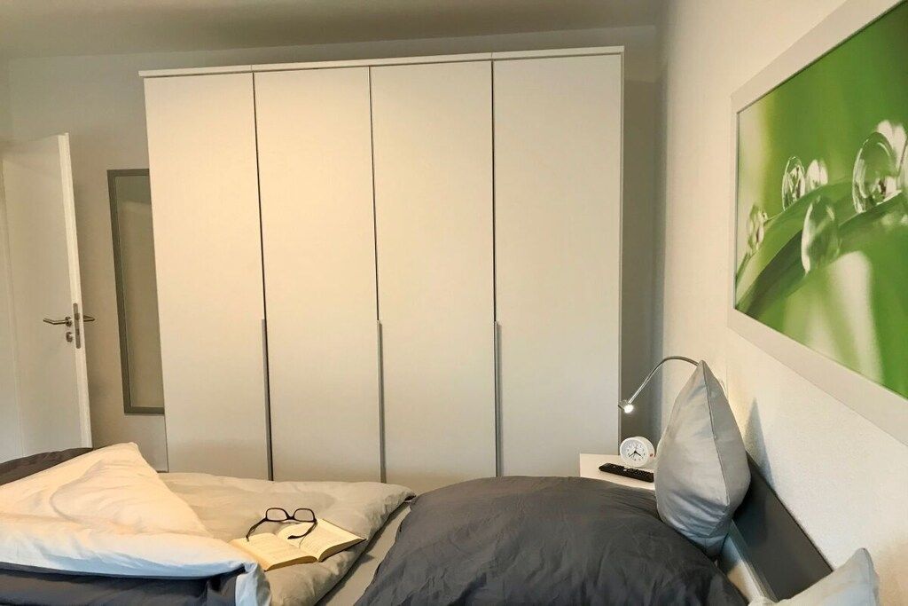 Un dormitorio con una cama, una mesita de noche con lámpara, un armario y un cuadro con marco verde en la pared.