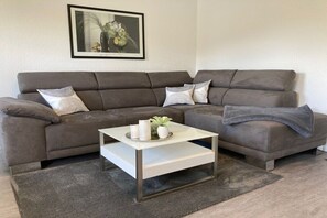 Ein Wohnzimmer mit einem Ecksofa, einem Couchtisch und einem gerahmten Bild an der Wand.