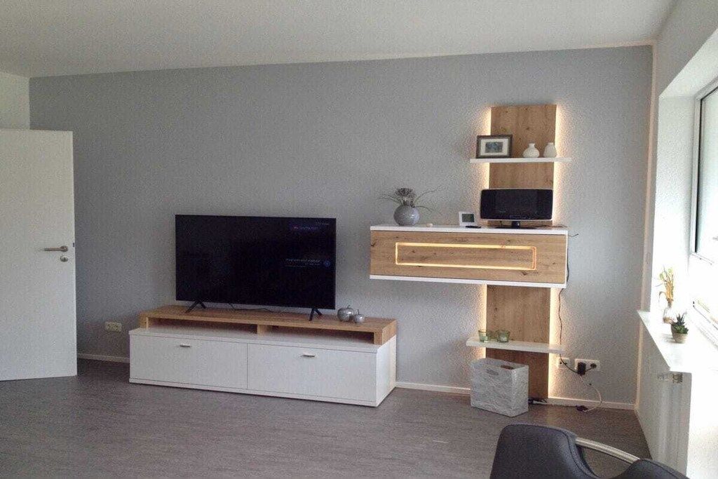 Ein modernes Wohnzimmer mit Flachbildfernseher, einer Holzunterhaltungsecke und einem weißen Schrank.