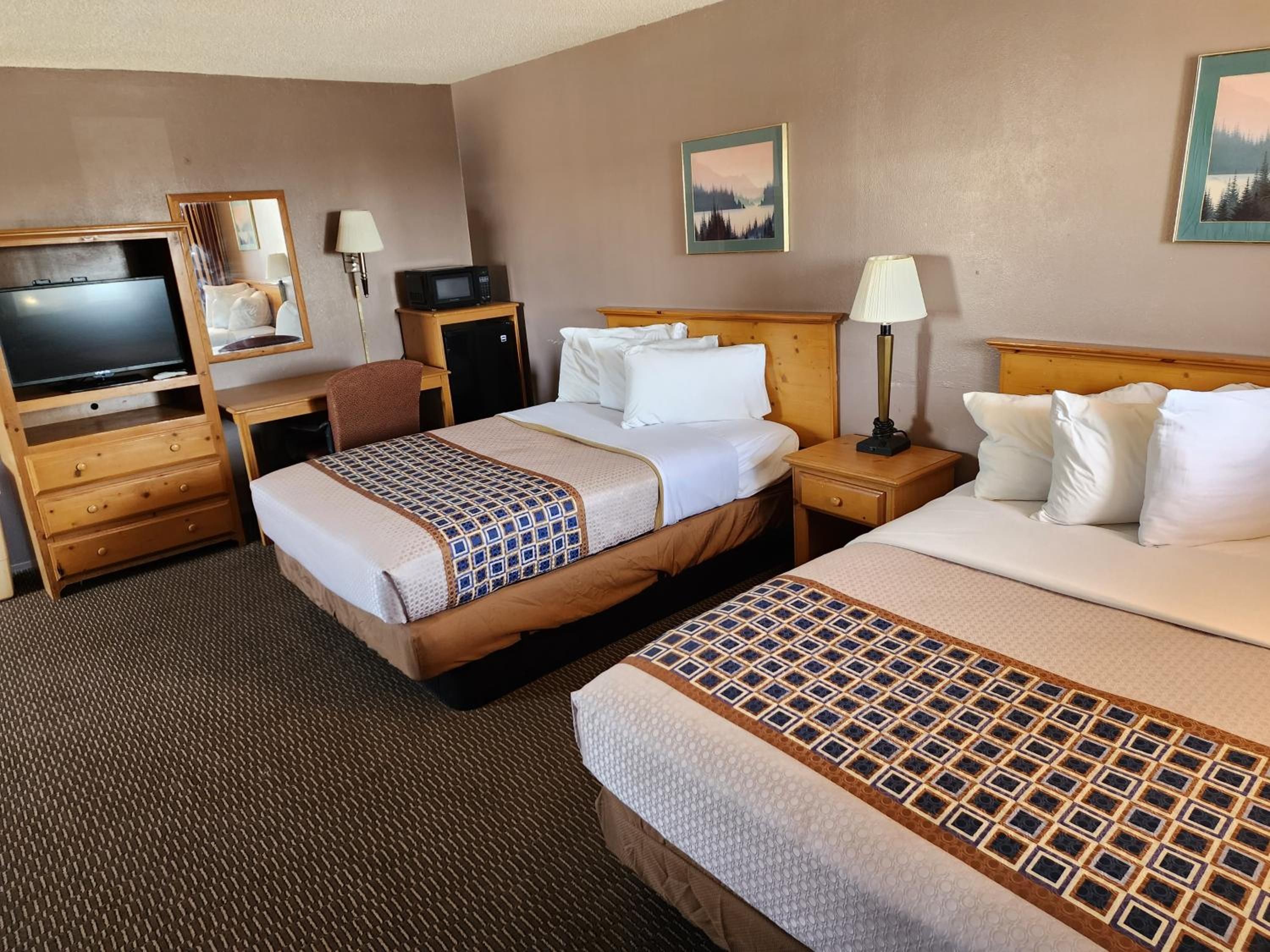 Habitación de hotel con dos camas, un escritorio con ordenador, televisor y espejo.