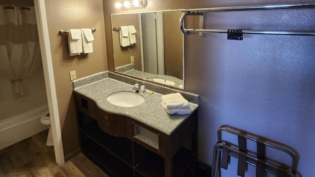 A bathroom with a sink, mirror, towel rack, and a shower area. - Rodeway Inn (Alamogordo)