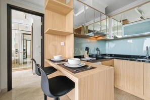 A modern kitchen with wooden cabinetry, a black chair, and a dining table set with white plates and bowls. - Karion by Kozystay - Menteng (Central Jakarta)