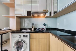 A modern kitchen with a built-in washing machine, wooden cabinets, and a black countertop. - Karion by Kozystay - Menteng (Central Jakarta)